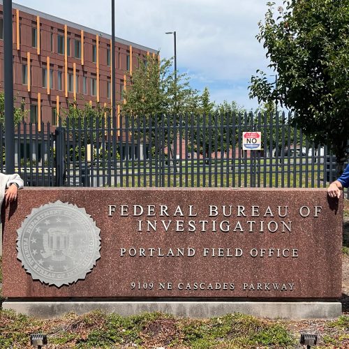 Man and woman stand to either side of a large sign that reads Federal Bureau of Investigation