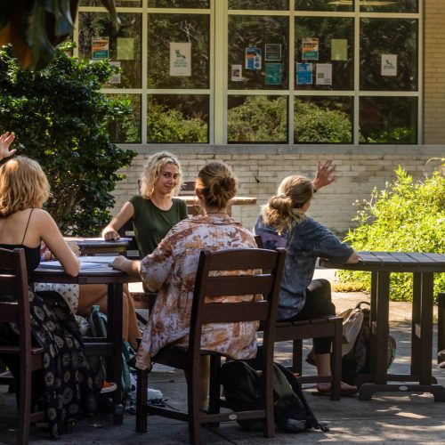 Students seated at a table outside a building while professor sits opposite them smiling