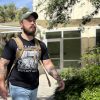 Young bearded man in t-shirt and cap with tattoos walking down pathway into building