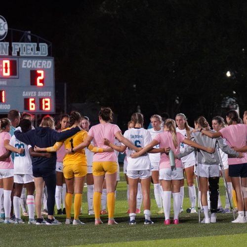 Team huddle on the field with some players in pink jerseys and the scoreboard reading 2-2