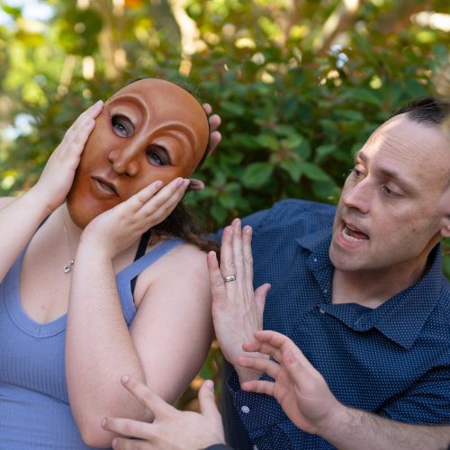 Student wearing mask puts hands to face while theatre professor and student encourage her