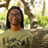 Student wearing glasses stands in front of an old oak tree