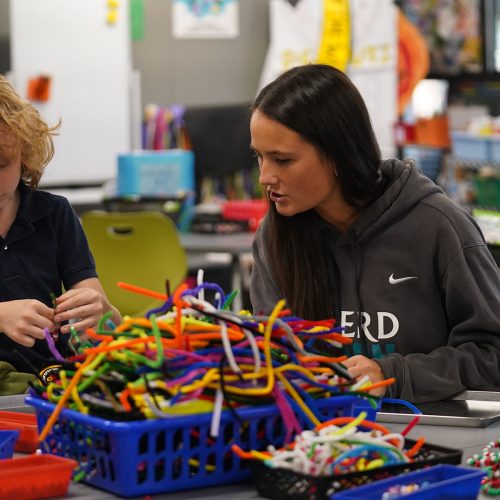 College student in a sweatshirt that reads Tritons helps a pupil