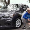 Student squats beside his car with water in background