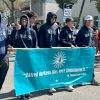 Five students in sweatshirts that say TRITONS hold a banner while walking down a street