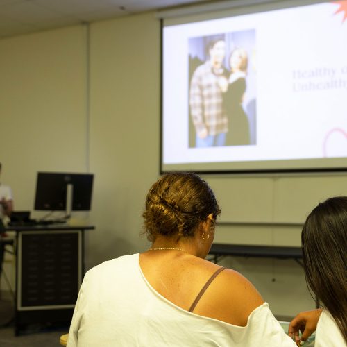 Two students look at materials before them as a lecturer presents on a screen that shows a heart