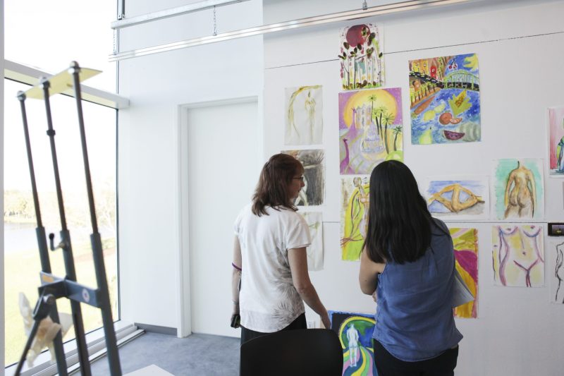 Two students standing by easel and looking at art on a wall