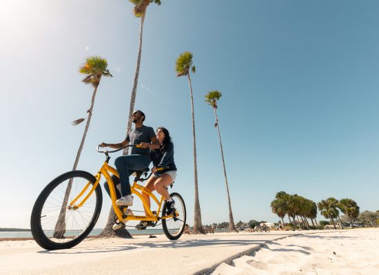 Eckerd students ride a tandem yellow bike along the beach